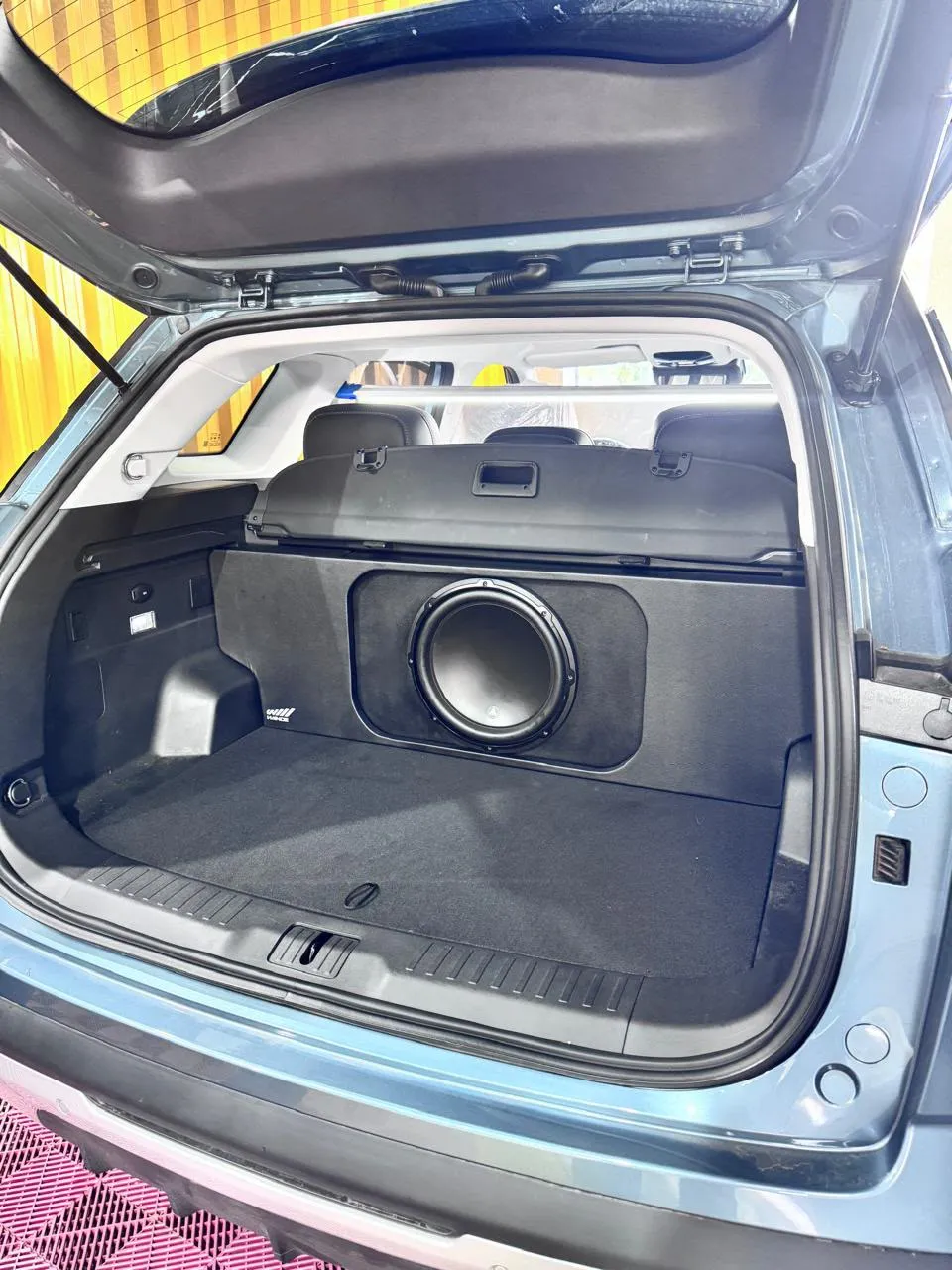 Porta-malas de SUV azul com caixa de subwoofer sob medida e acabamento em carpete