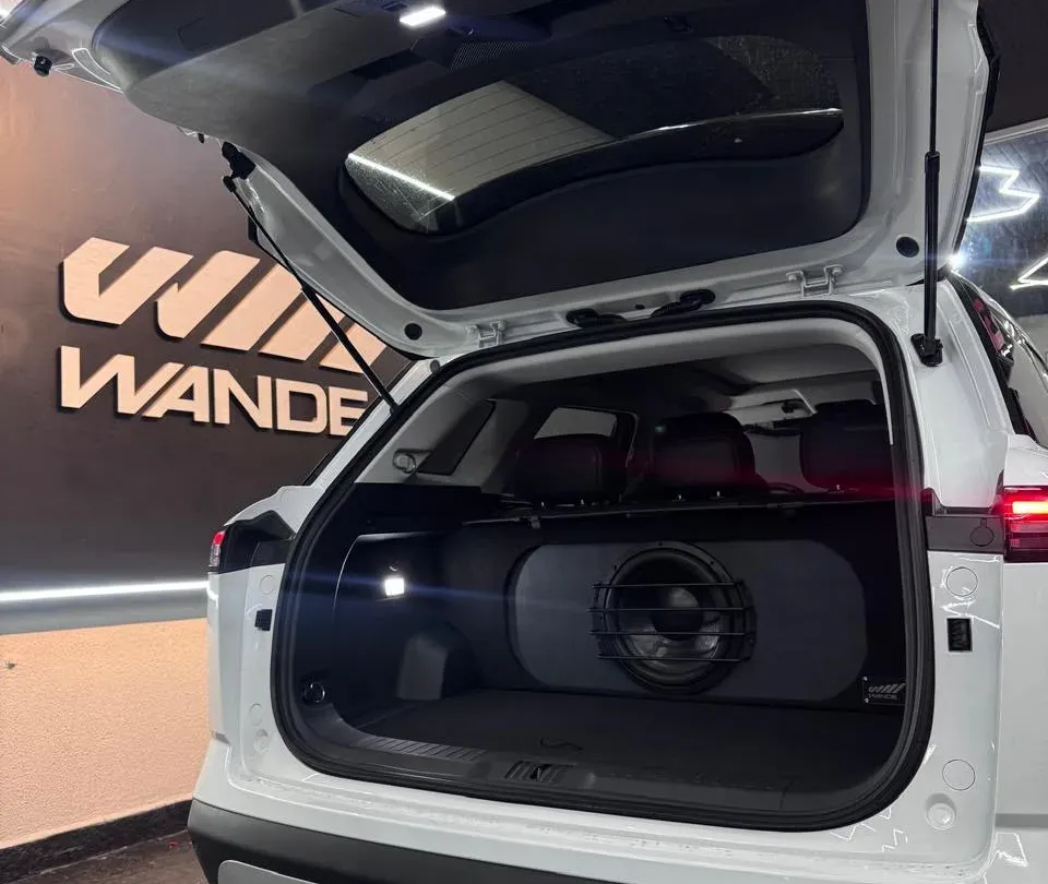 SUV branco com subwoofer em caixa sob medida no porta-malas, em frente ao letreiro da Wande