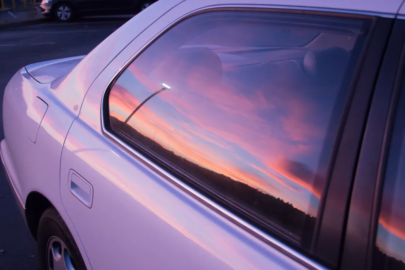 Céu do entardecer refletido no vidro lateral de um carro